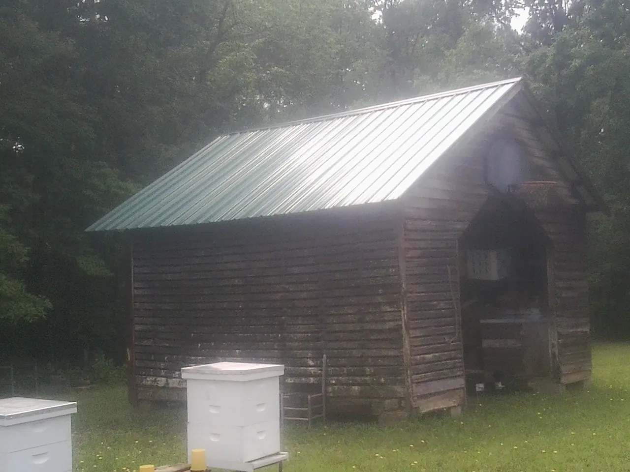 Green metal roof on a weathered barn beside stacked beehives in Sparks
